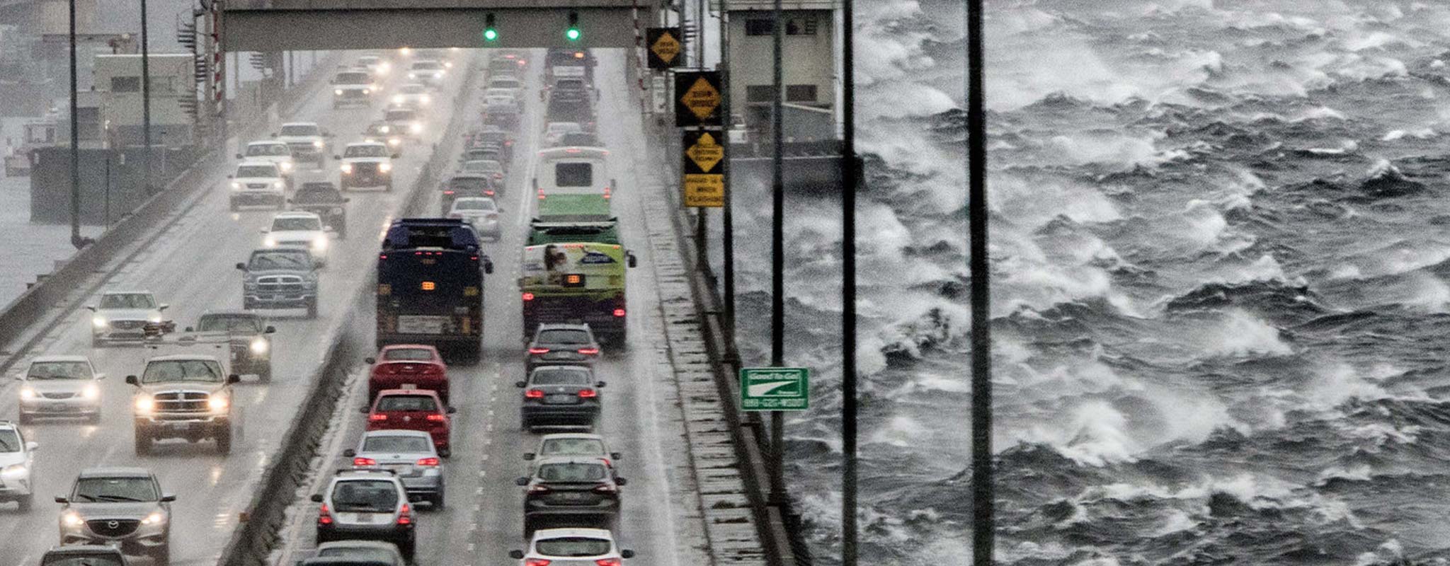 Cars driving over bridge in high winds with white caps on the water.