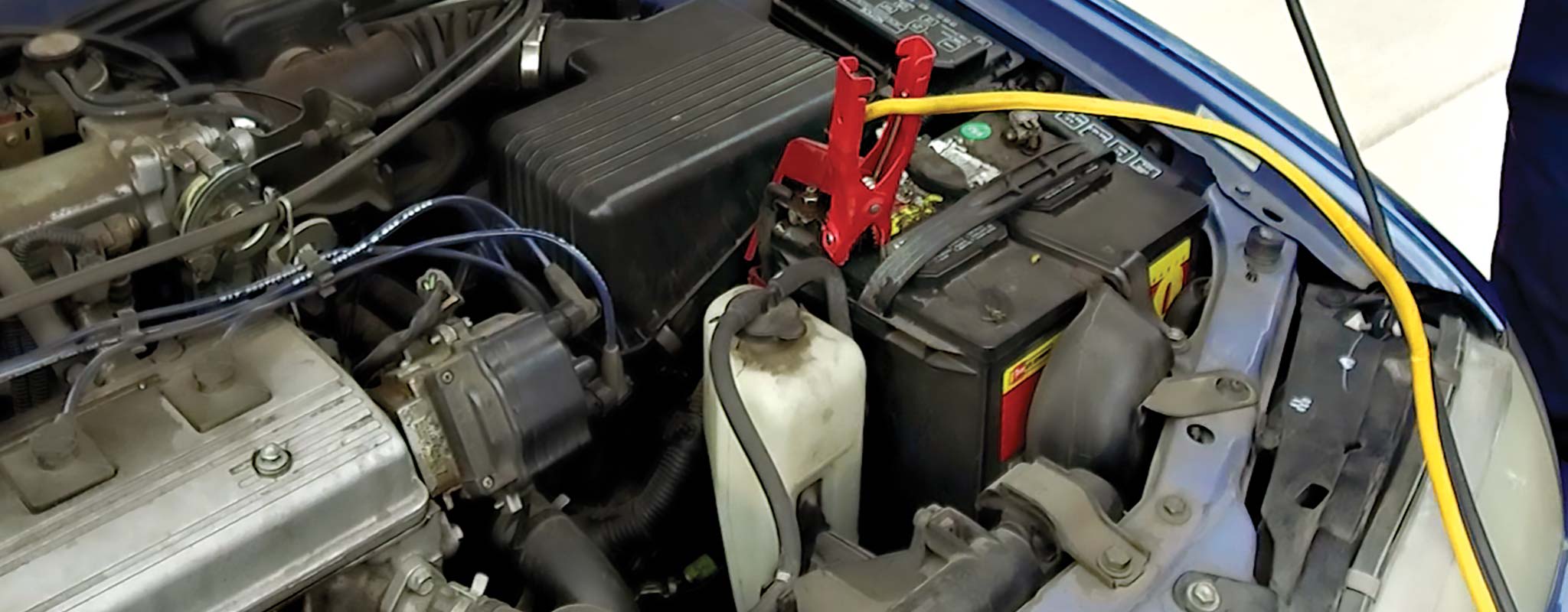 A car battery under the hood with jumper cables attached.