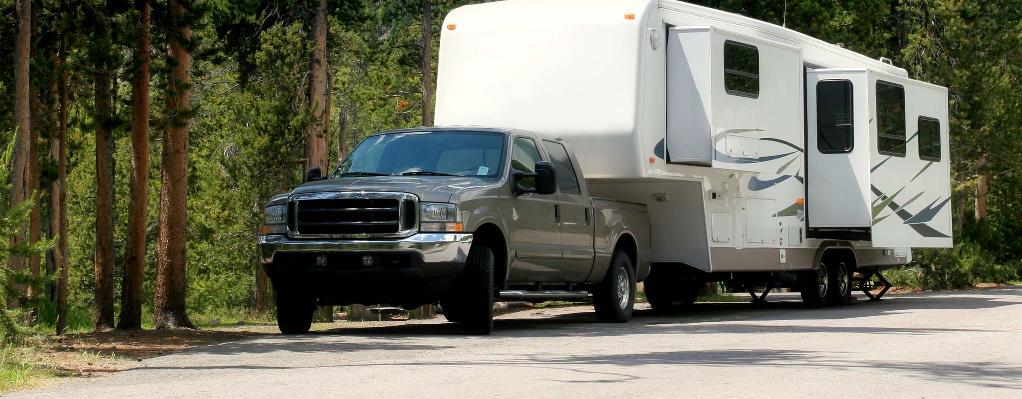 A truck and travel trailer parked in a forested campground.