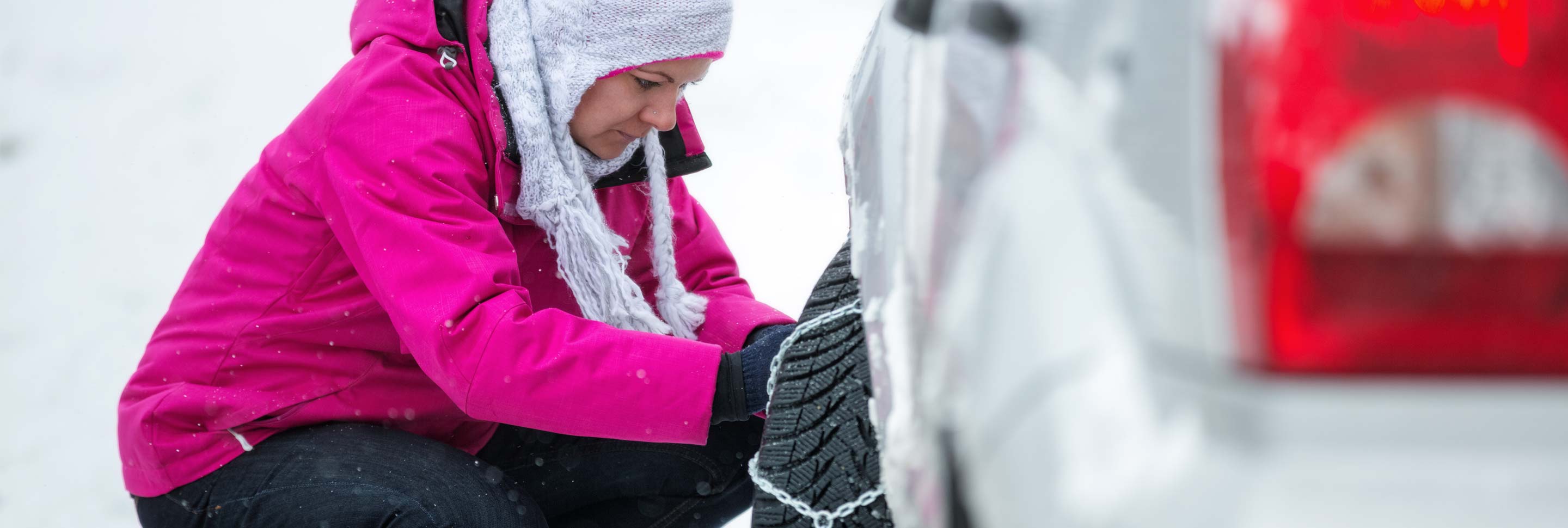 A woman putting chains on her snow tires.