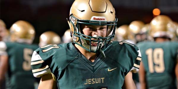 A Jesuit high school football player in front of his teammates, garbed in colors of gold and green.