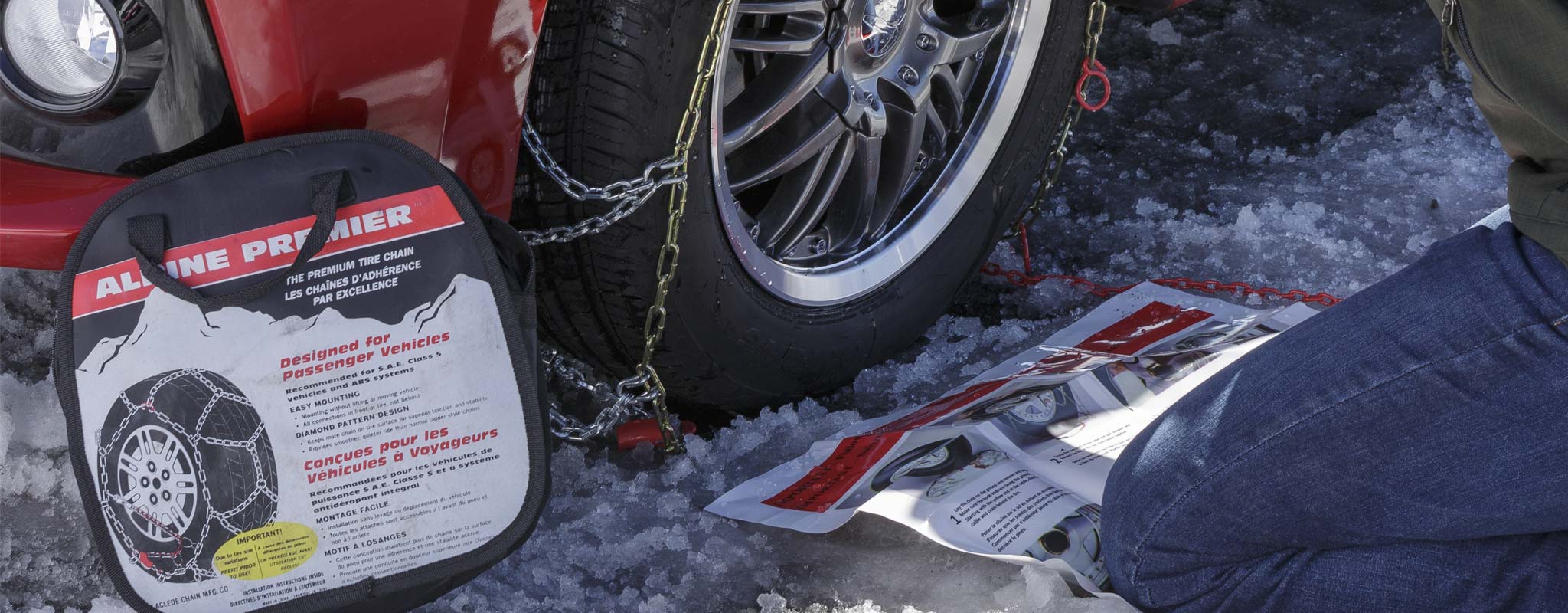A person putting snow chains on their passenger vehicle.