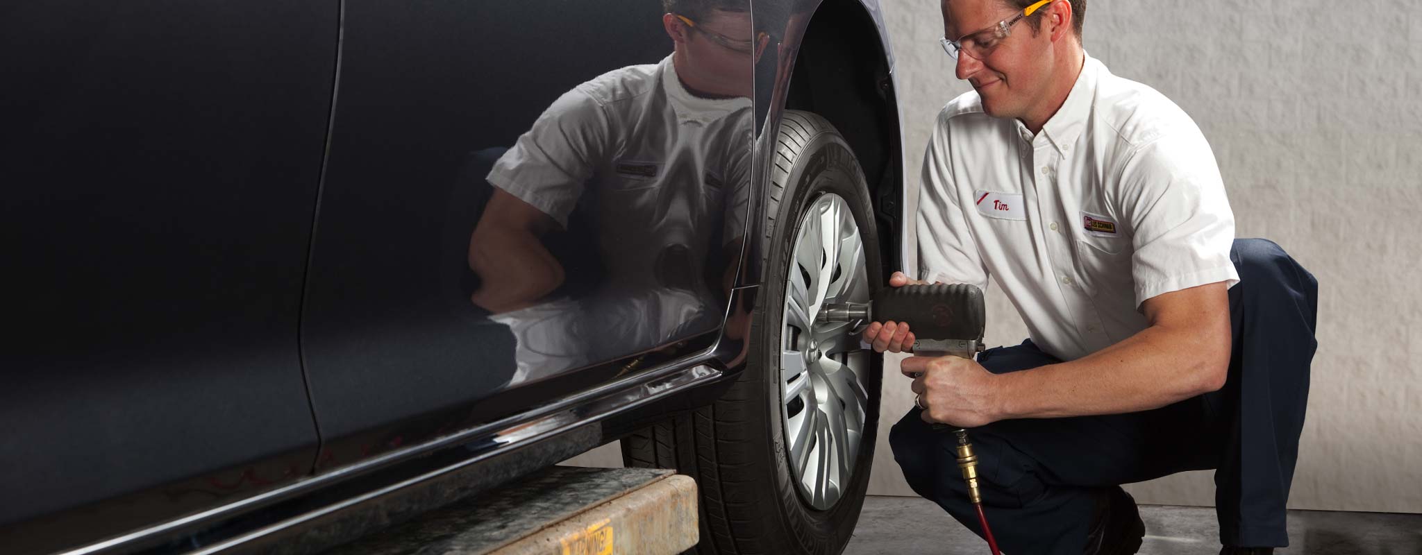 A tire technician using an air gun to remove lug nuts from a tire.