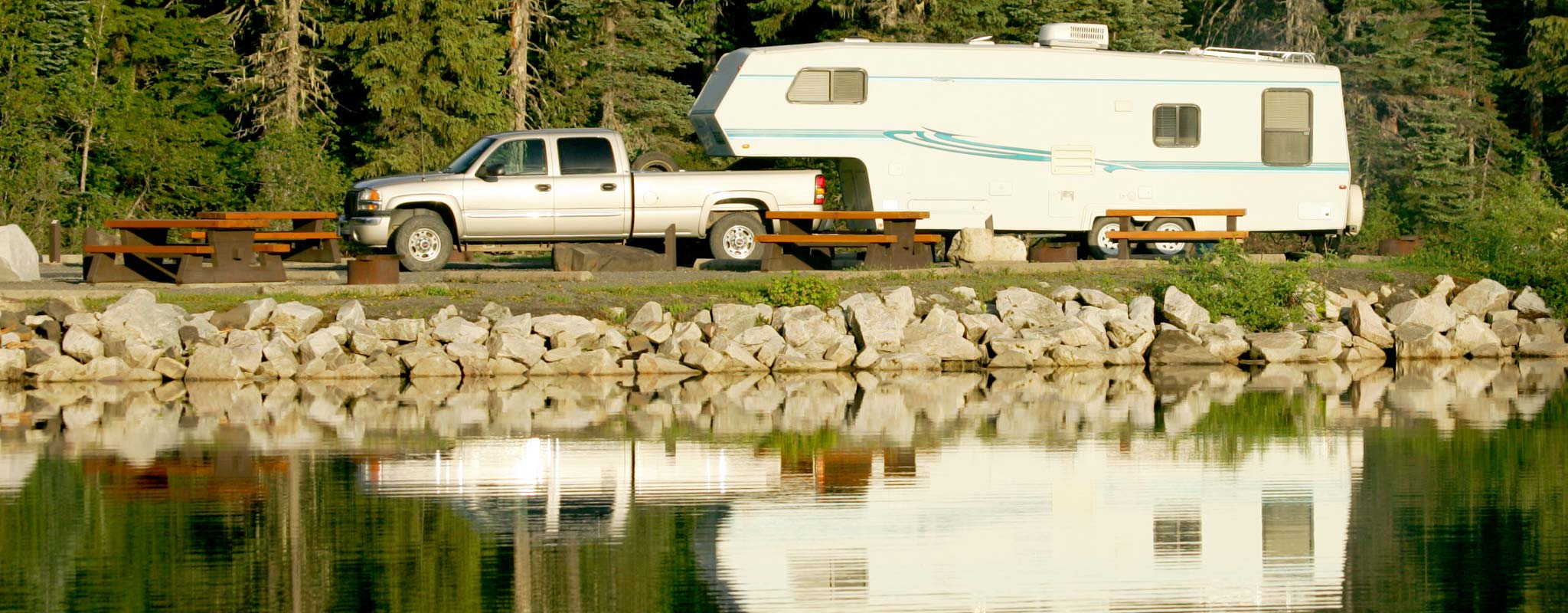 A pickup with a fifth wheel travel trailer parked in a campground next to a lake.