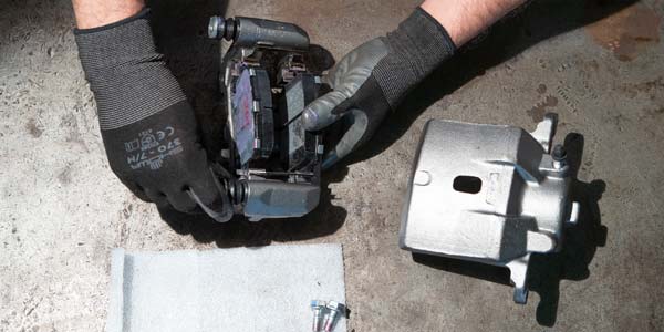 A Les Schwab technician adding new brake pads to a remanufactured brake caliper.