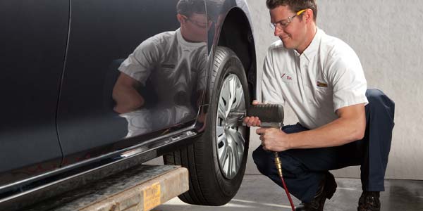 A tire technician using an air gun to remove lug nuts from a tire.