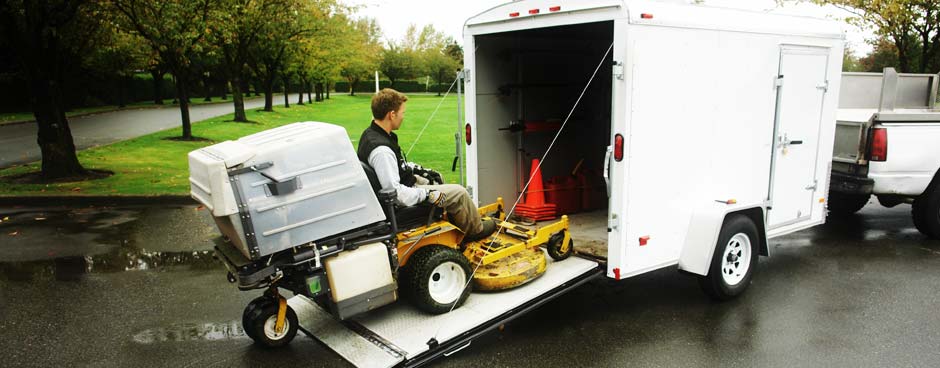 A landscape worker drive a riding lawnmower into a trailer.