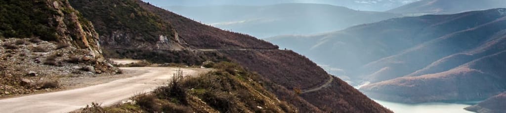 A twisting road cut into the side of a mountain, with a steep dropoff to the river below.